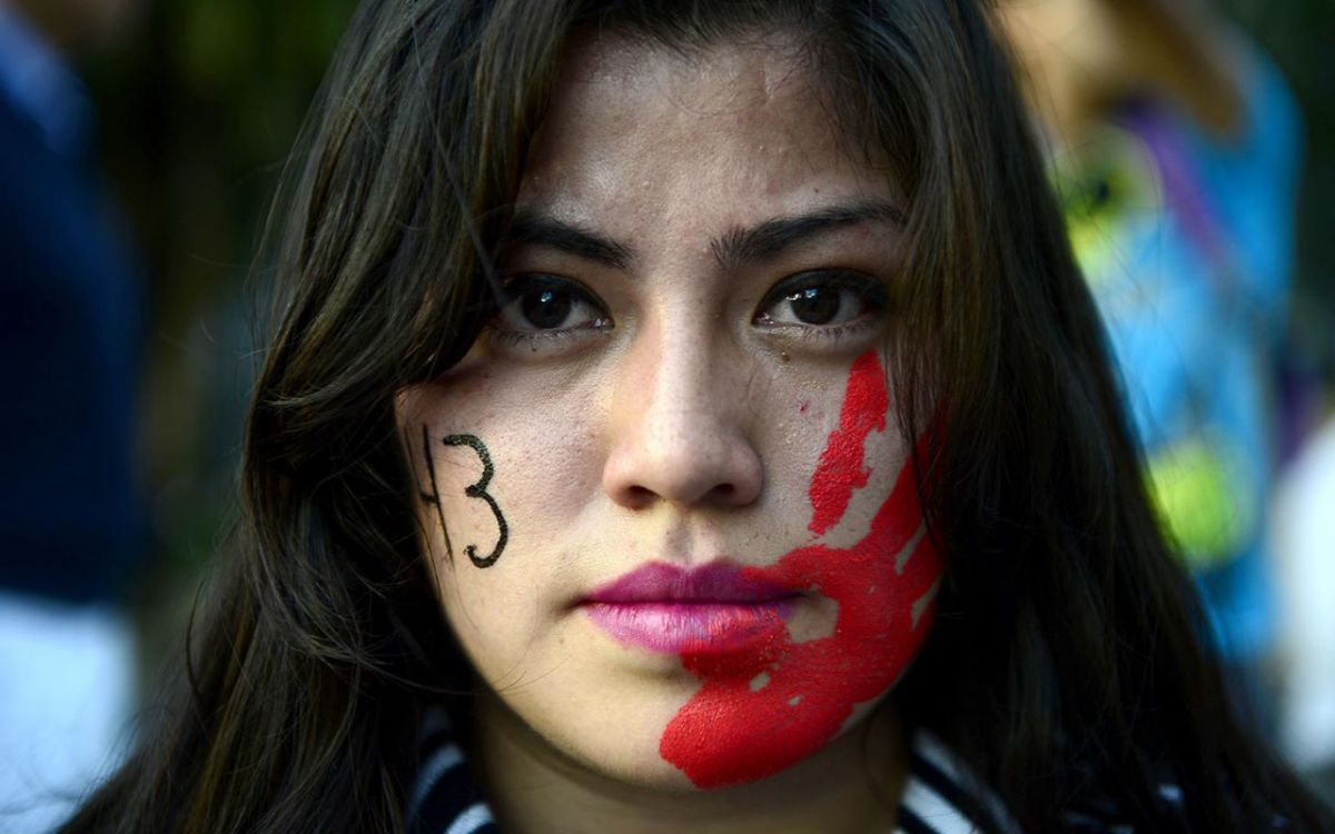 A woman protests, the body count and blood marked on each side of her face.